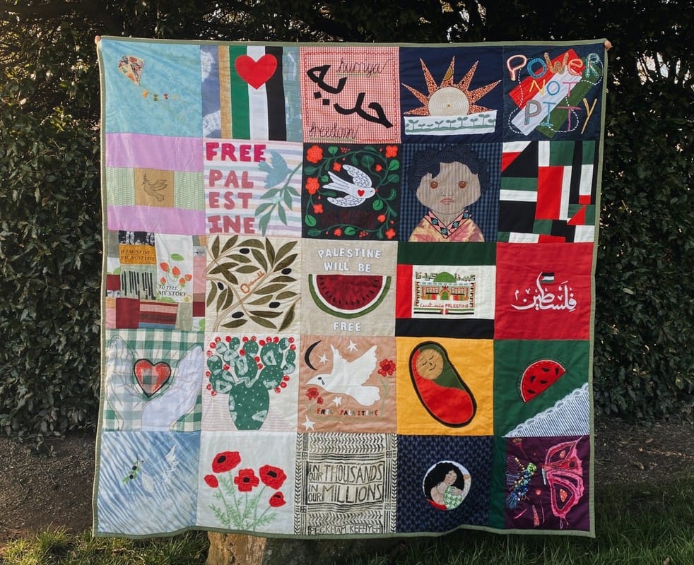 A quilt made of 25 blocks, each with a message or image in solidarity with Palestine: poppies, children, watermelon, the words "Power Not Pity," etc.