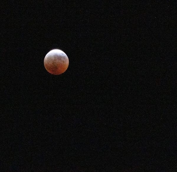 A full moon, silvery-white along the top curve with a deep red cast on the bottom half, against a black sky.