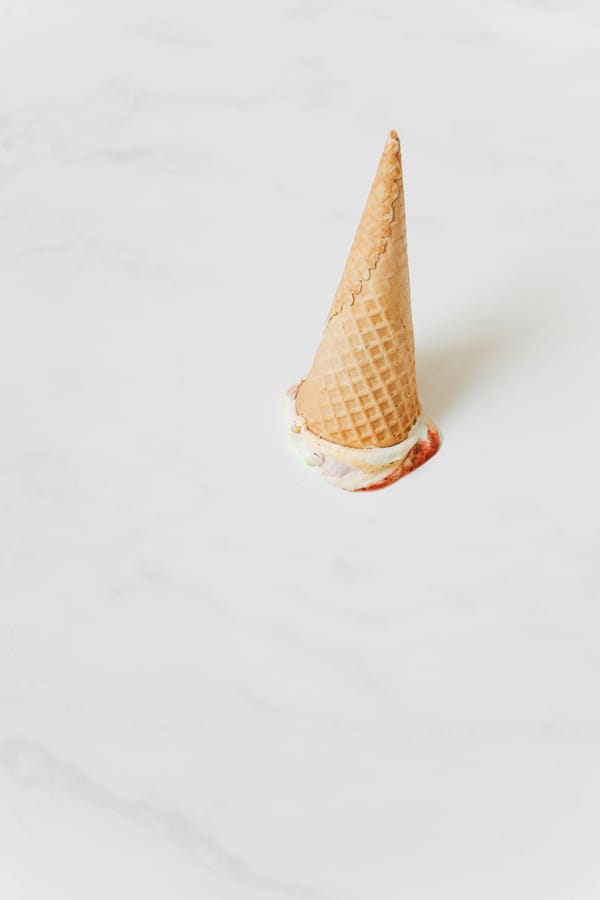 An otherwise perfect-looking ice cream cone upended on a white marble surface. The scoop is smooshed.